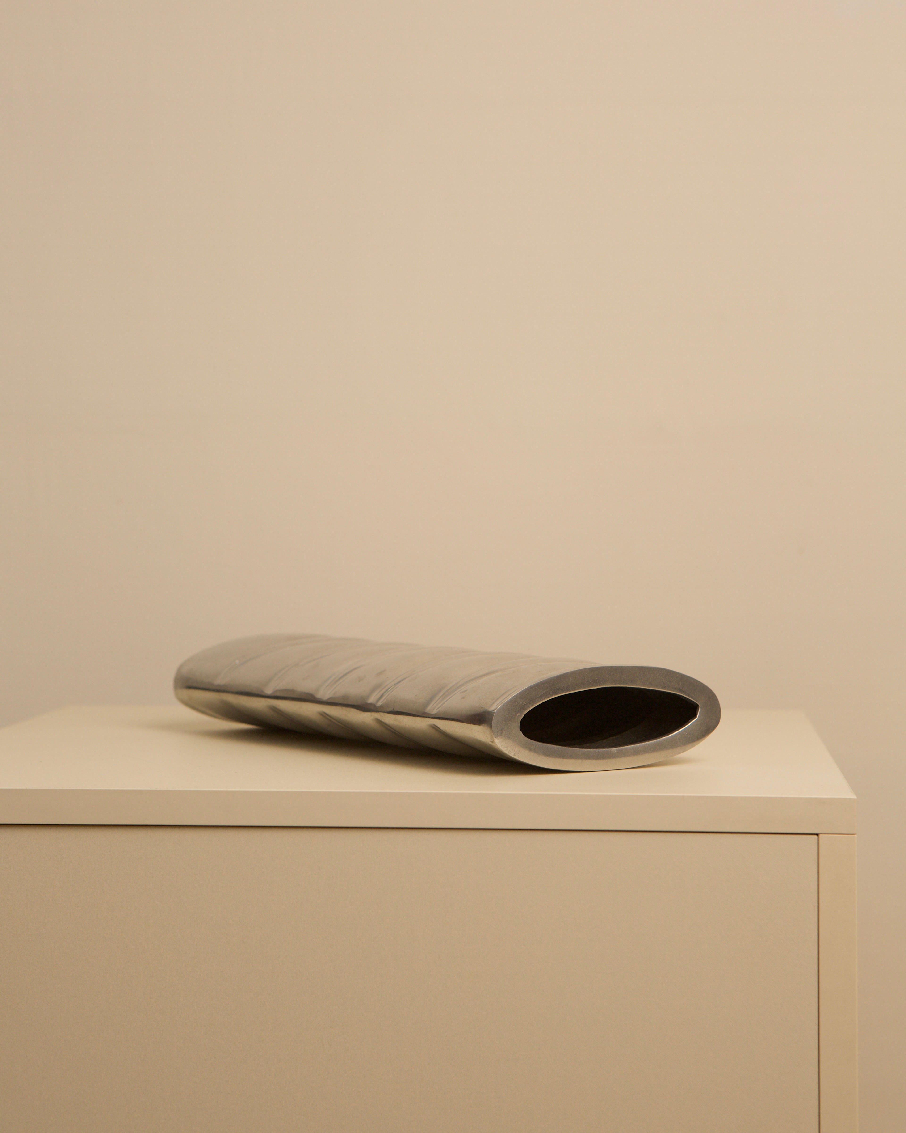 Curved aluminum vase with oval opening on minimalist display
