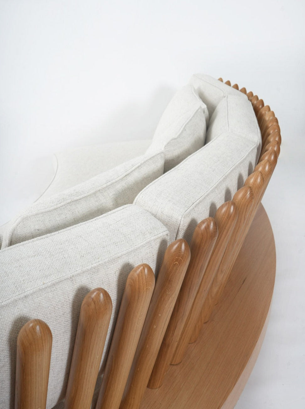 The San Romano Round Oak Sofa by Barracuda Interiors features light beige cushions, an oval wooden base, and rounded oak rods along the backrest for a sculptural, stylish look.