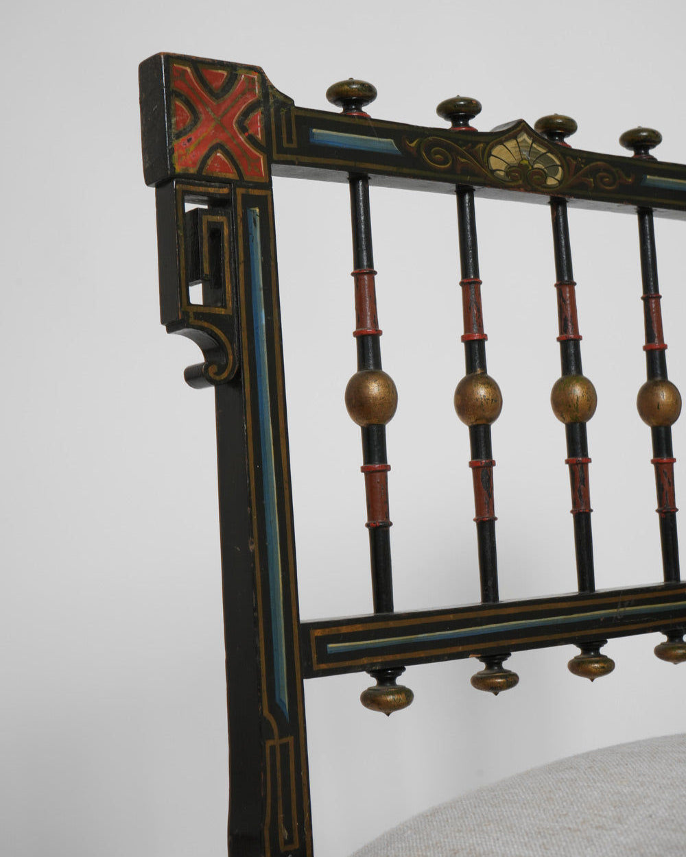 Close-up of a Napoleon III Painted Armchair (19th c.) by Barracuda Interiors, featuring geometric red, blue, and gold patterns on the back, vertical spindles with gold and red spheres, and a light upholstered seat.