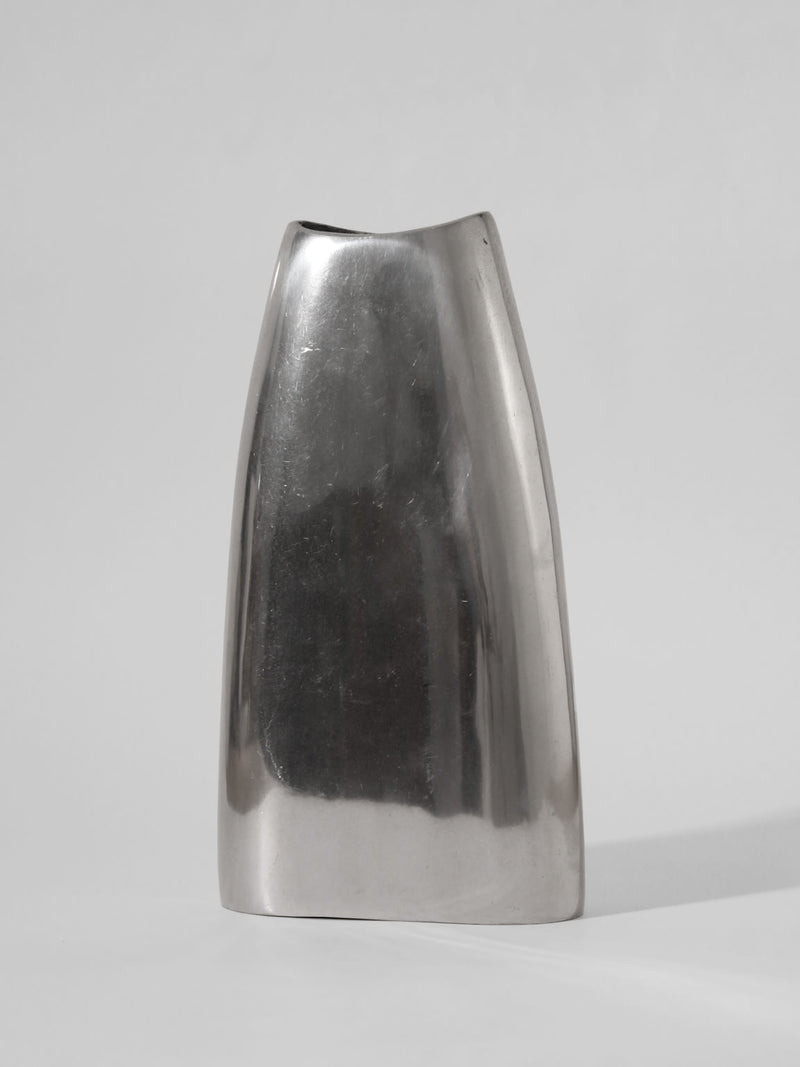 The Polished Aluminum Flat Tall Vase by Vintage Stories features a minimalist, silver finish and sleek asymmetrical design from 1960s Germany, shown against a plain light gray background.