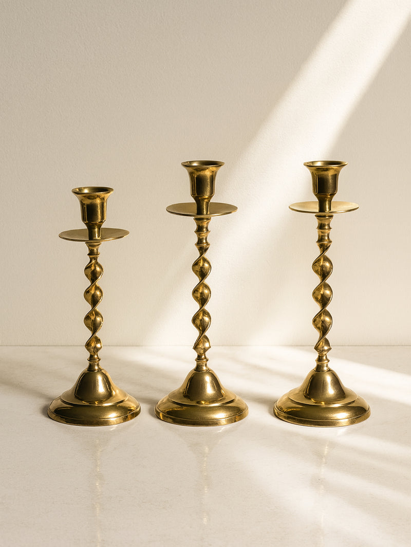 Three brass candlesticks with twisted stems on marble surface