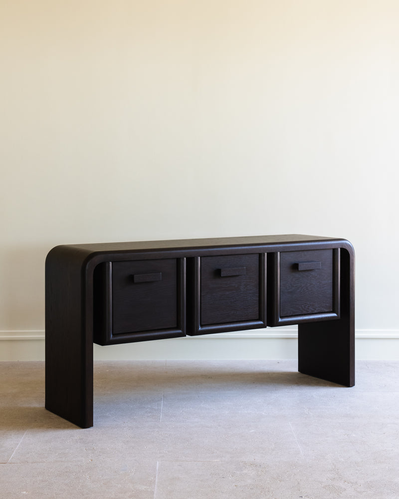 Dark wood console table with three curved drawers and rounded edges