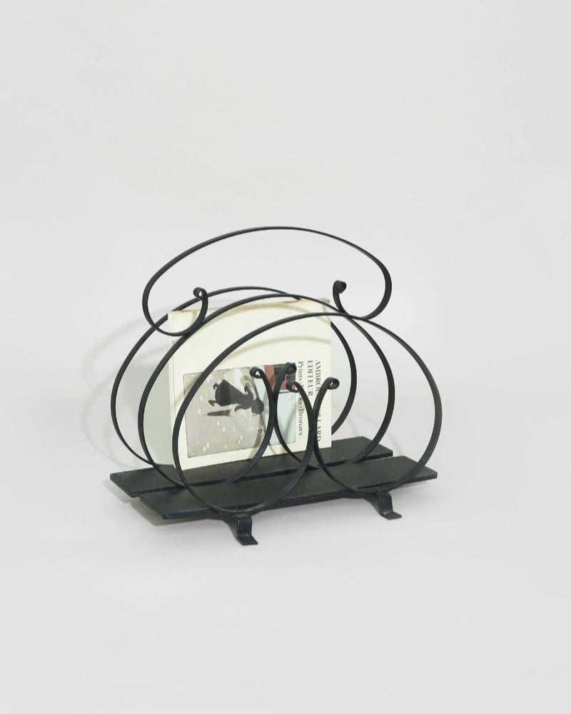 Black iron magazine rack with curved metal frame on rectangular base