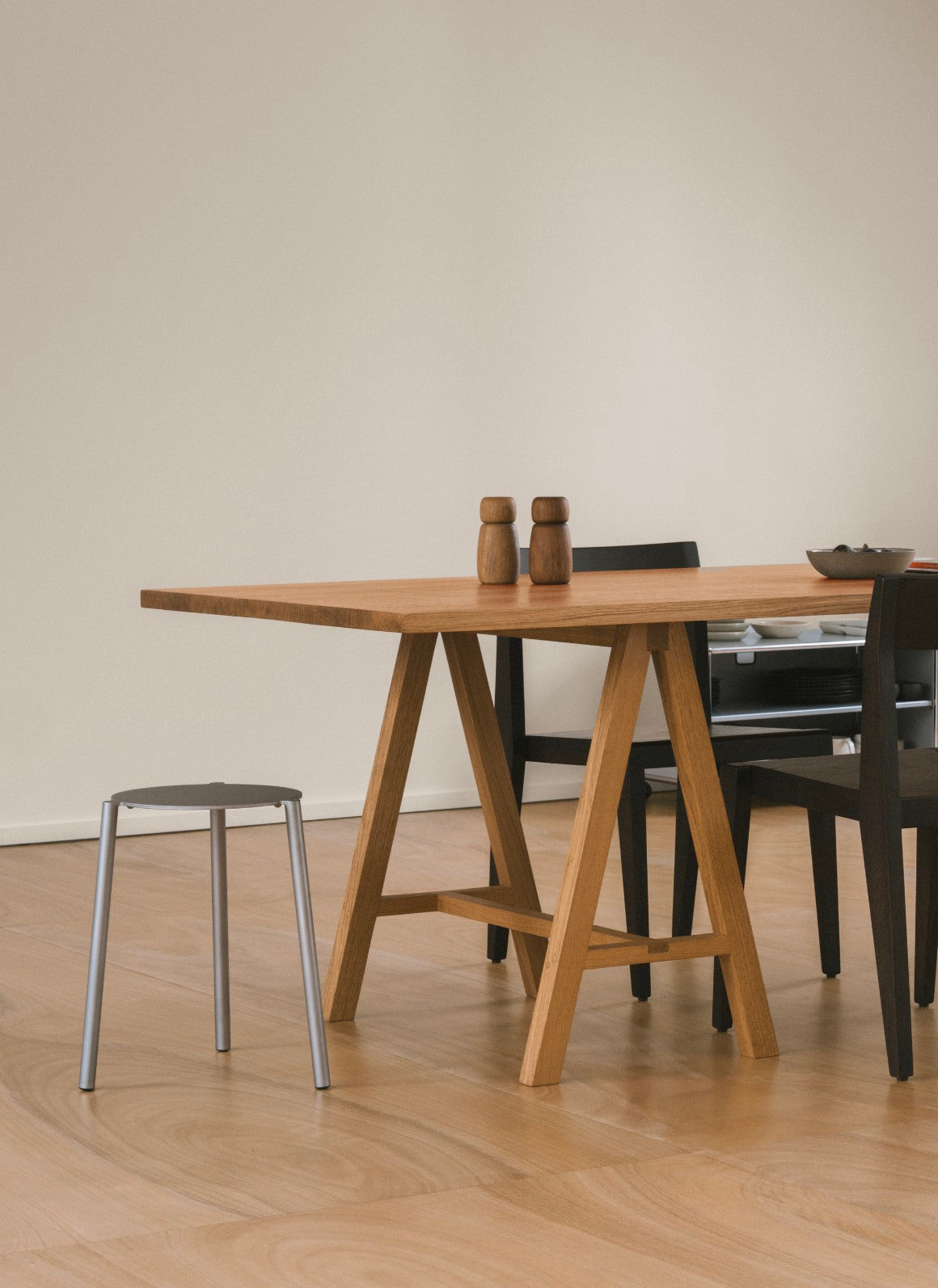 Stool - Isla x Paul Delrez - Stainless Steel — side view beside wooden table