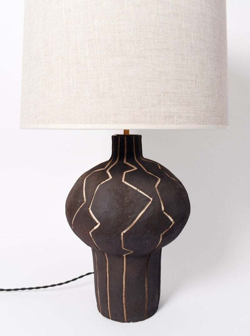 The "Lanzarote" Lamp by Barracuda Interiors features a black ceramic base with textured beige lines and a large round beige fabric shade, offering customizable lighting for your space.