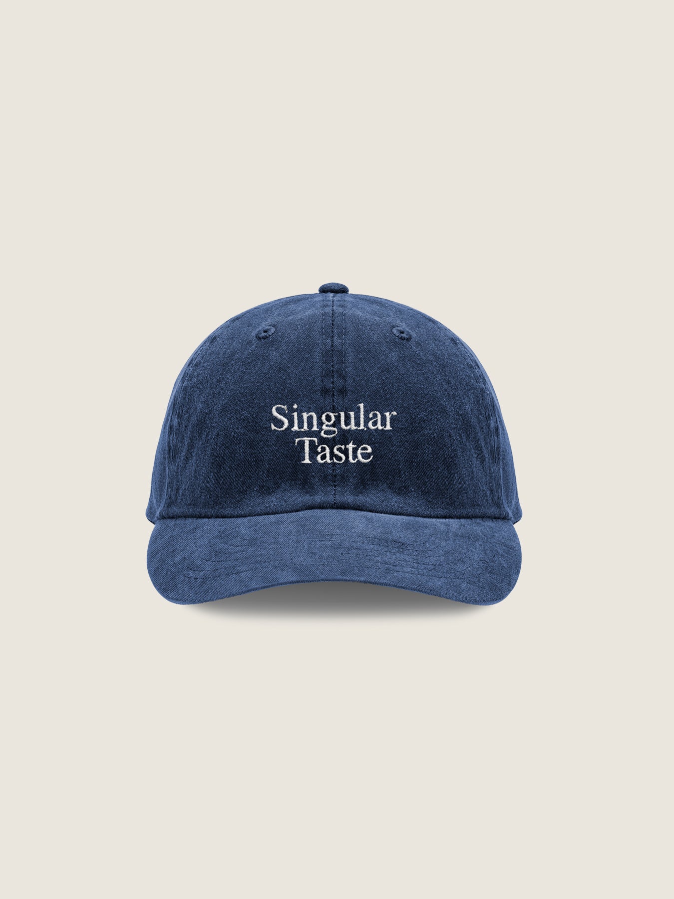 The Singular Cap by The Oblist is a blue baseball cap with "Singular Taste" embroidered in white on the front, featuring an adjustable back strap for a perfect unisex fit, set against a plain, light background.