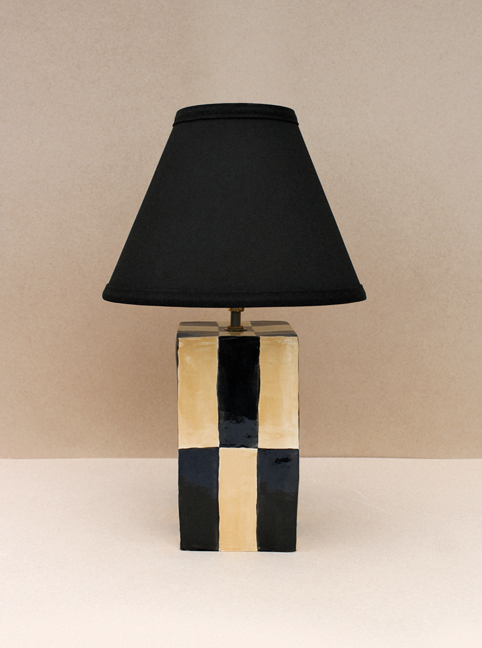 A contemporary Socorro Lamp by Casa Veronica with a geometric, gold and black striped base and a custom conical black lampshade, set against a neutral beige background.