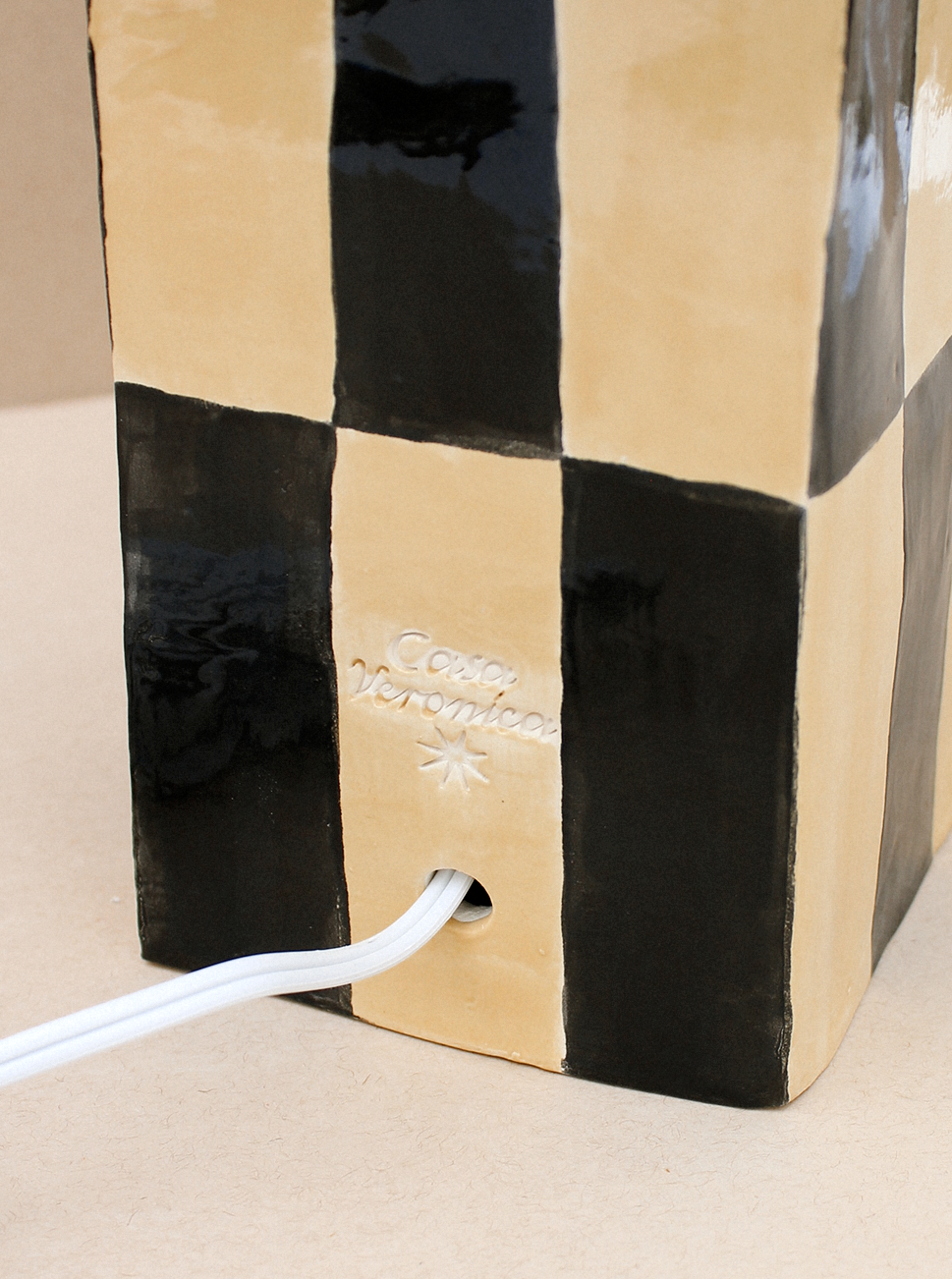 A striped black and beige ceramic Socorro Lamp base with the brand "Casa Veronica" embossed on it, featuring a white power cord extending from a brass socket at the bottom.
