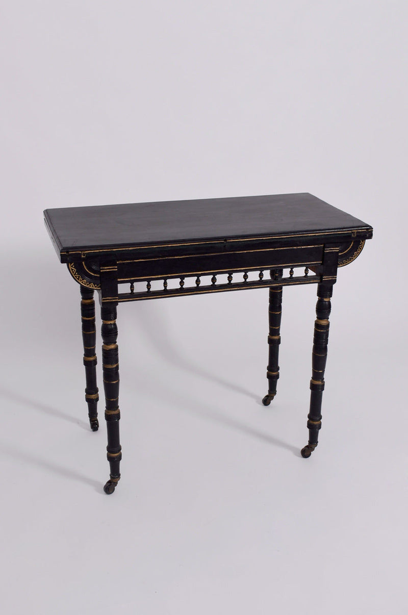 The Godwin Style Ebonised Table, 19th c. by Barracuda Interiors features spindle legs with small wheels and gold accents on the edges and apron, shown against a plain white background.