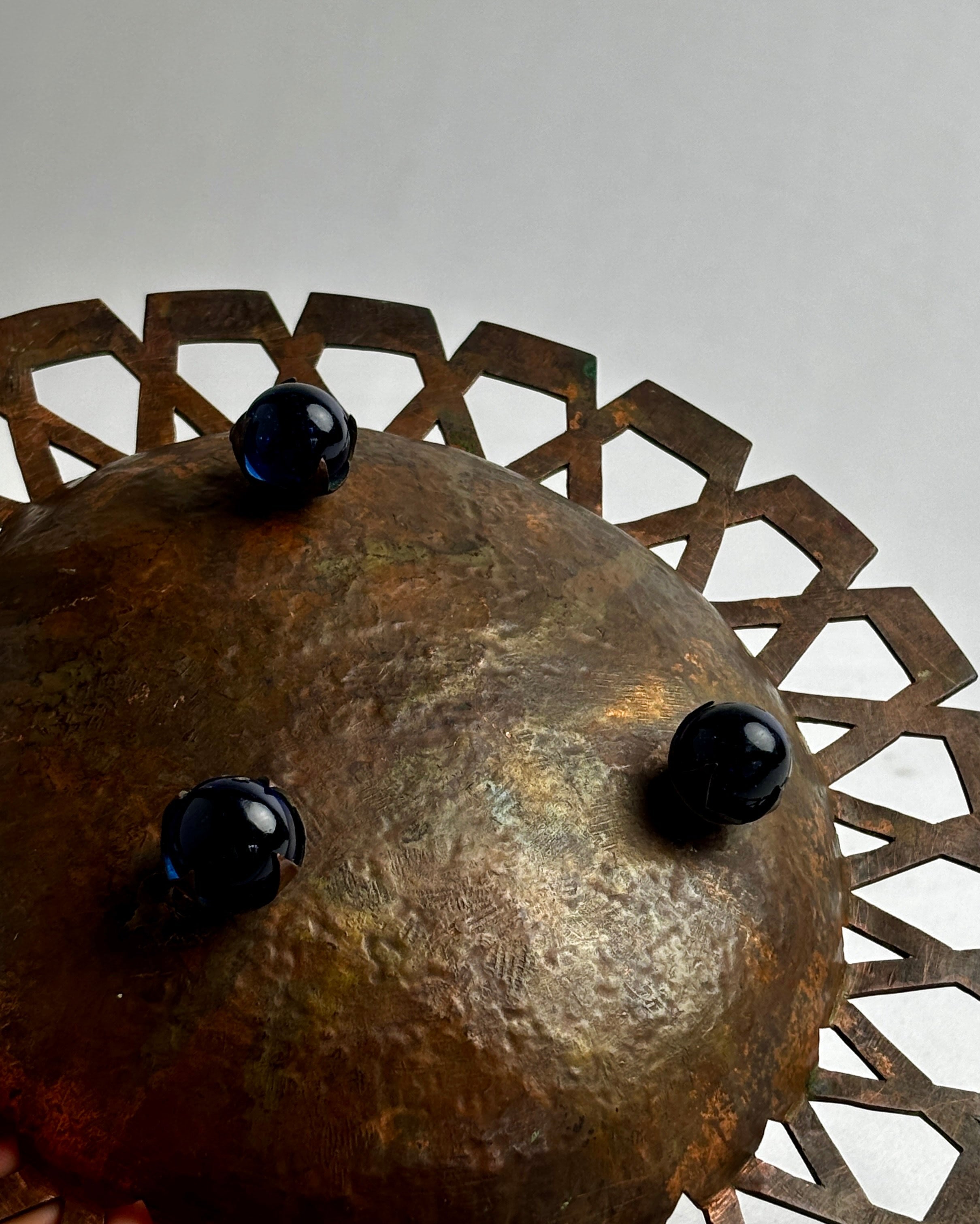 Detail view of hammered copper dish with decorative rim and dark spheres