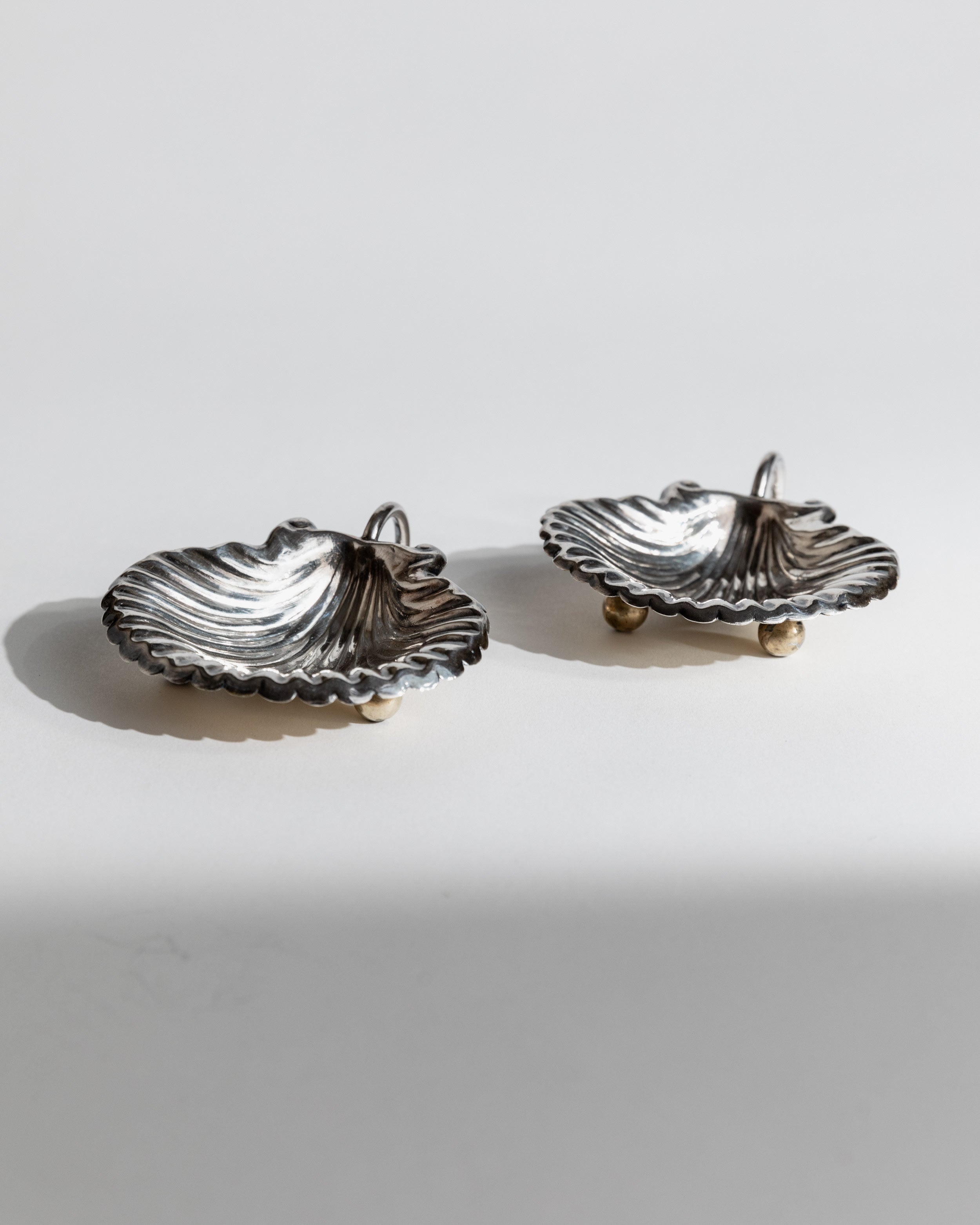 Two silver shell-shaped serving bowls with scalloped edges on feet