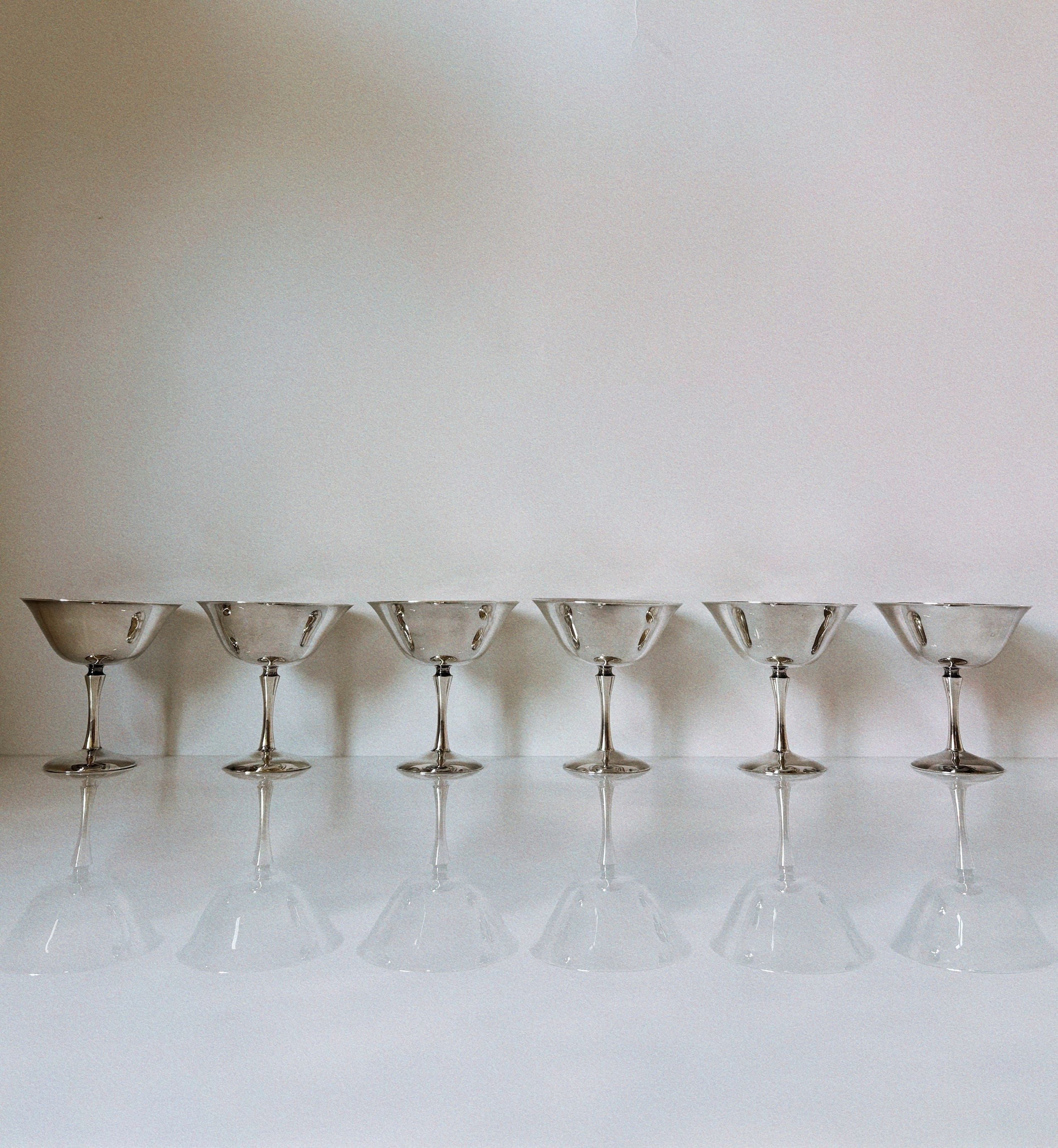 Six silver plated champagne coupes in perfect alignment on white surface