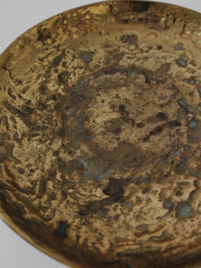 A close-up of the Massive Organic Textured Brass Bowl by Vintage Stories shows its round, uneven surface with rich brown, gold, and blue-green patina, highlighting the bowl’s aged and organic charm.