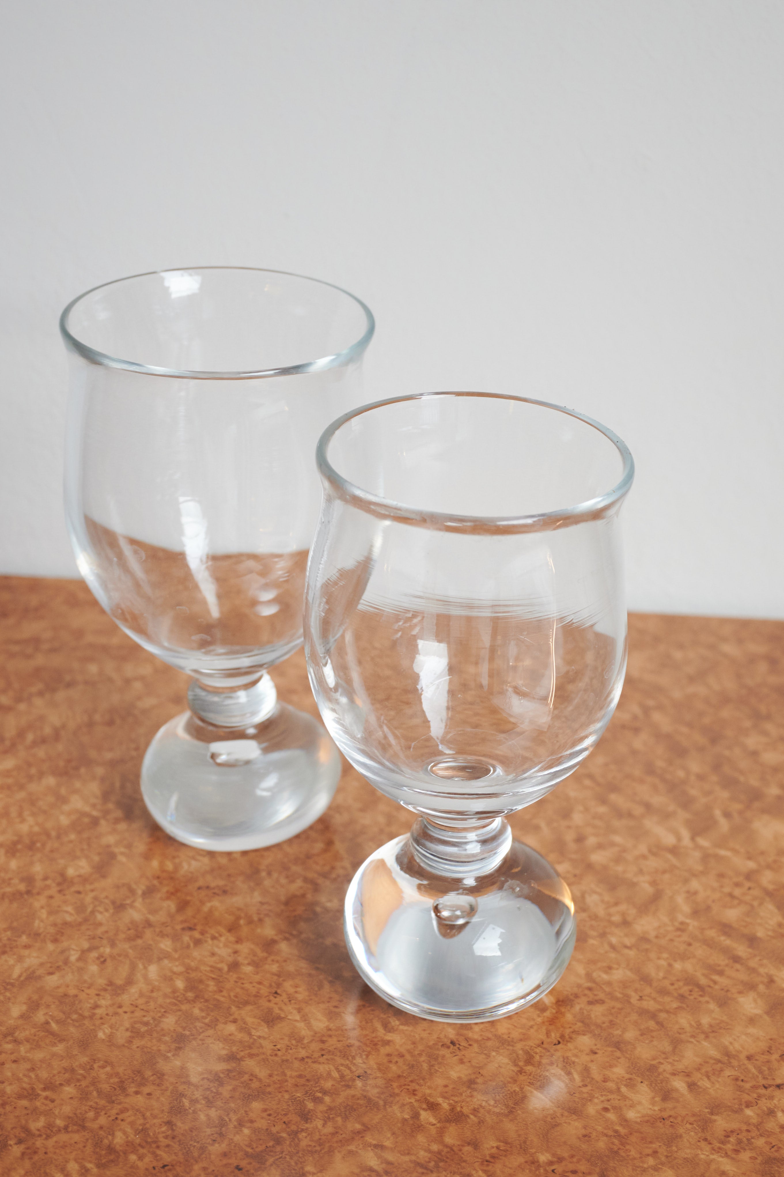 Two clear glass goblets with rounded bowls and pedestal bases on wood surface