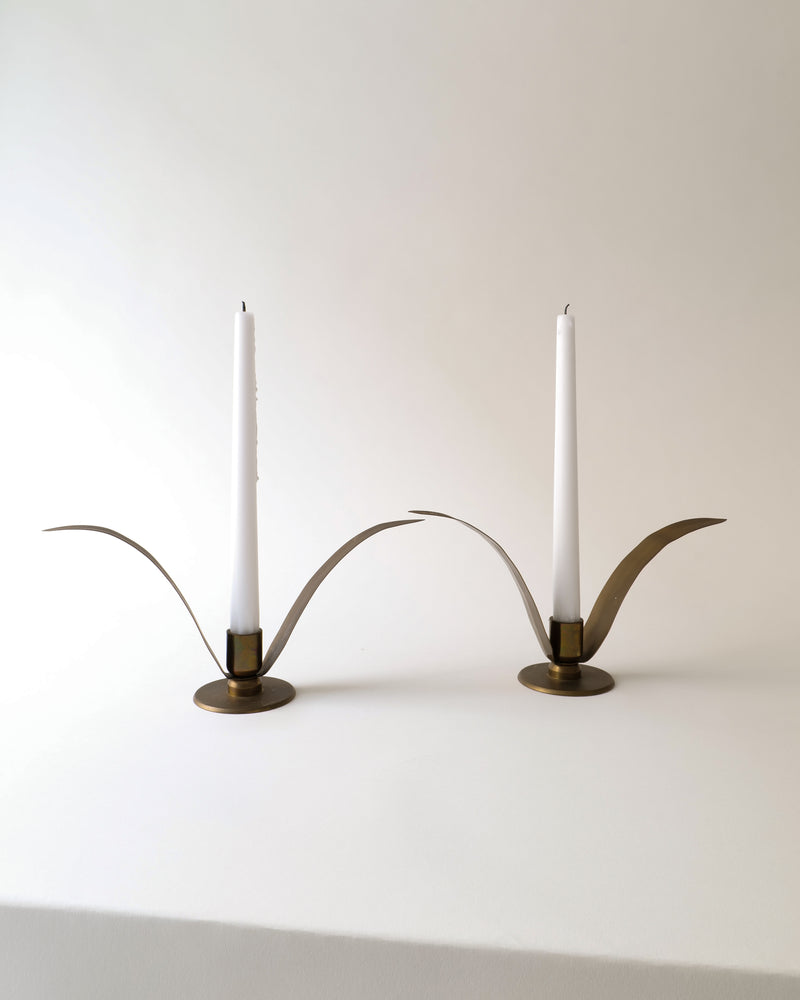 Brass candle holders with curved arcs and white candles, side view