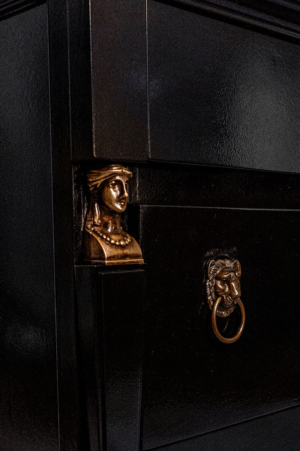 A close-up of Barracuda Interiors’ ‘Return of Egypt’ Lacquered Drawers, 19th c, showcases a black chest with a gold bust of a woman in jewelry and a lion head ring pull, capturing French elegance.