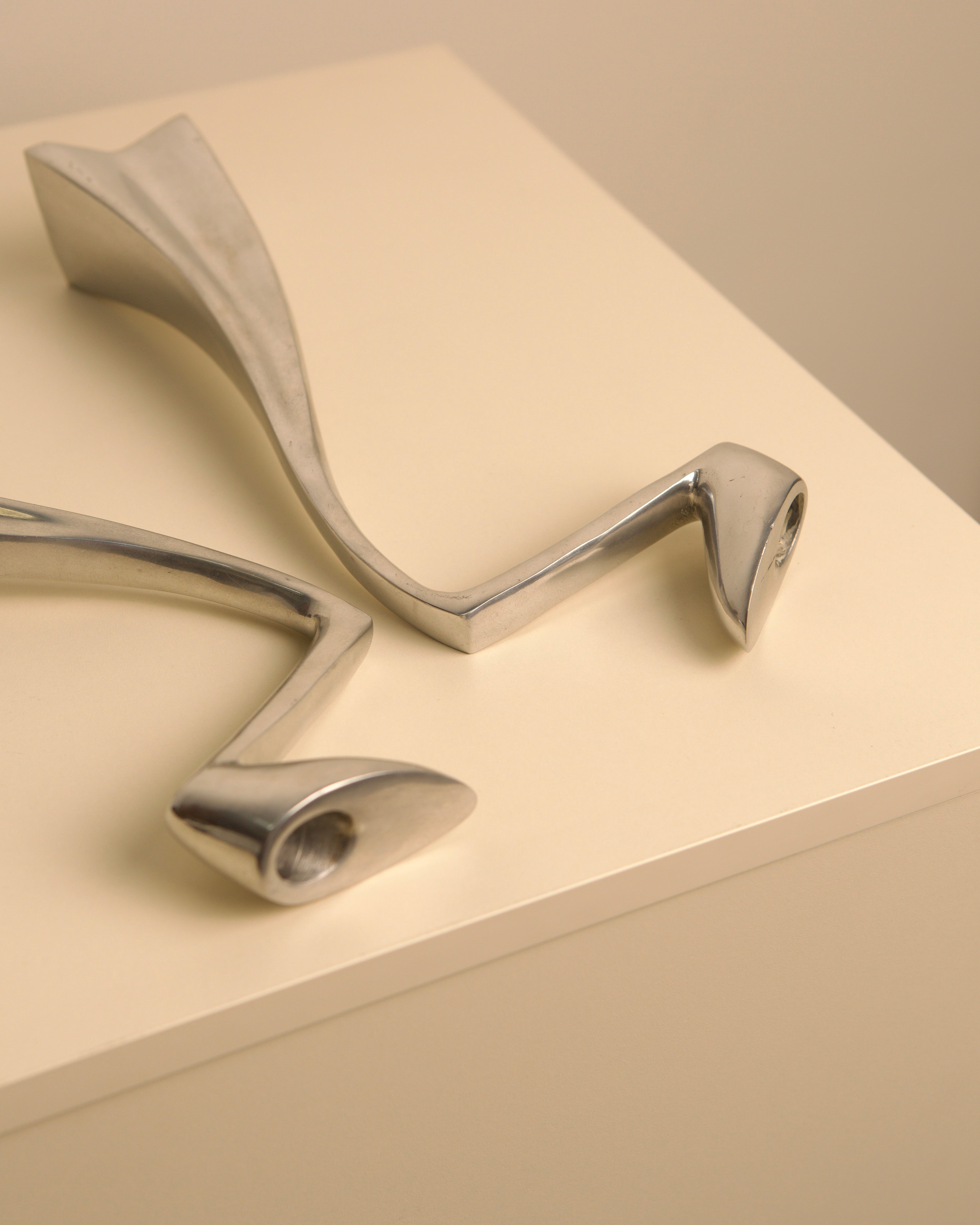 Paire de bougeoirs "Swan" par Matthew Hilton 80's — close-up of polished metal surface on neutral background