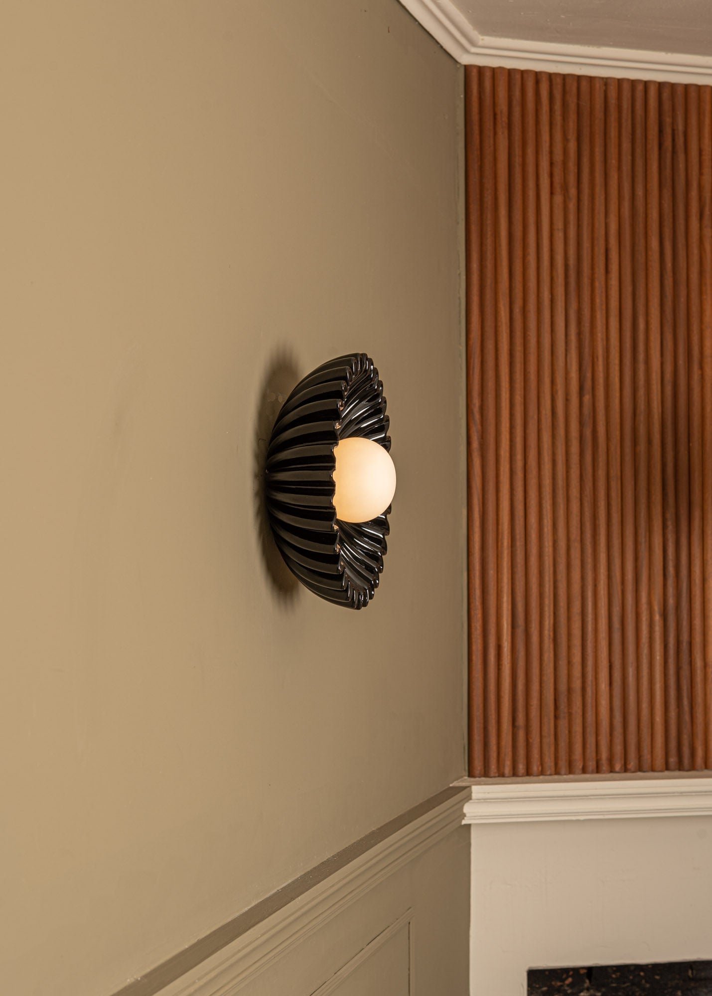 Black ceramic Ostro wall light with ribbed shell design installed