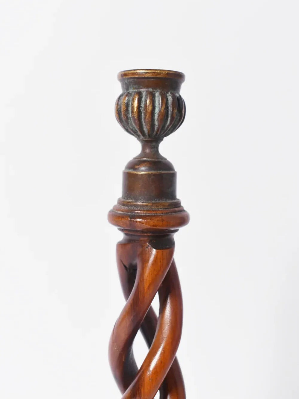 A detailed view of the Pair of Turned Wood Candlesticks, 19th c. by Barracuda Interiors shows intricate twisted carving and a decorative finial at the top, set against a plain white background.