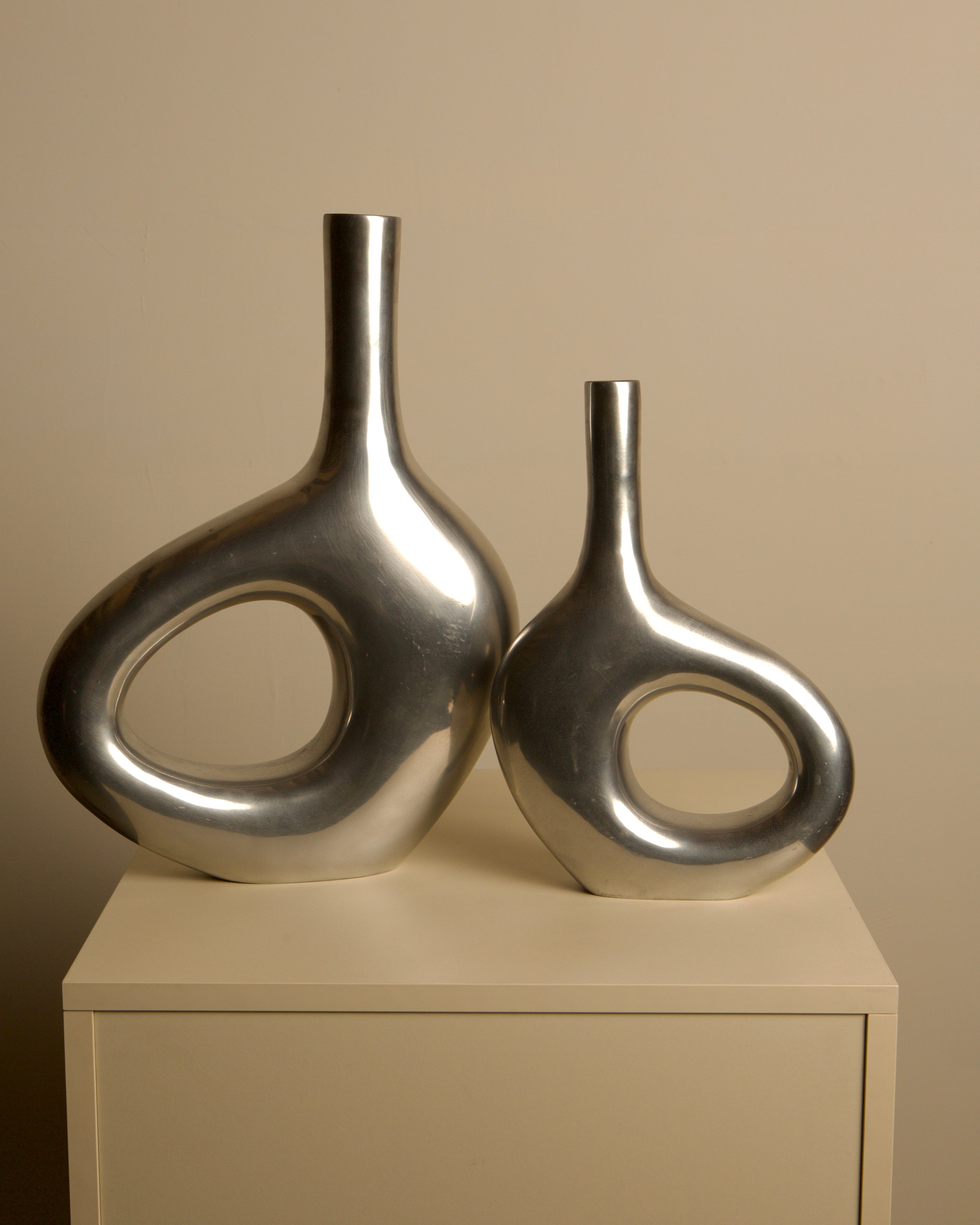 Pair of Italian cast aluminum vases from the 1980s — close-up of shiny silver surface on neutral background