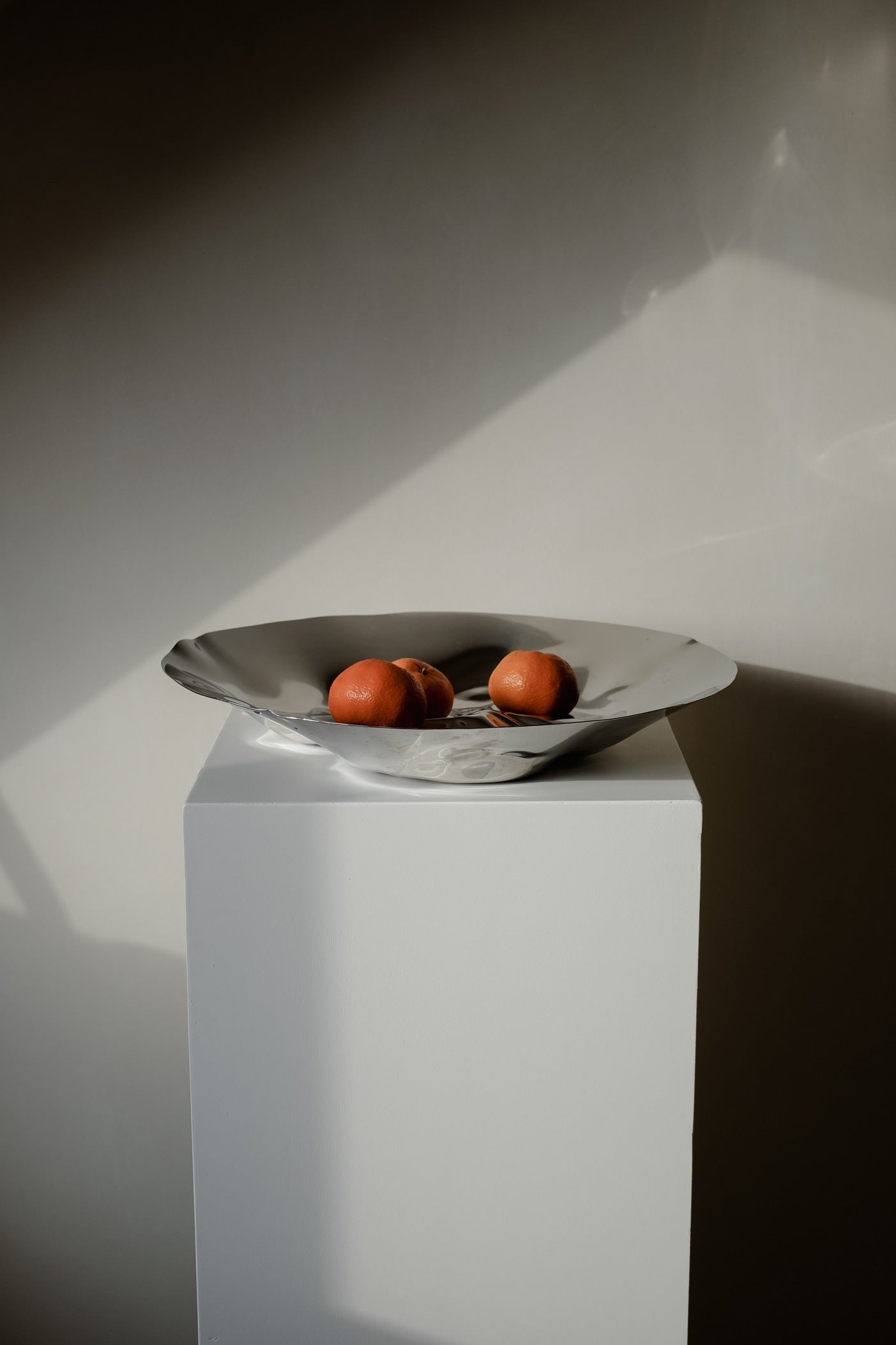 Chrome Curved Decorative Bowl — displayed on white pedestal with oranges