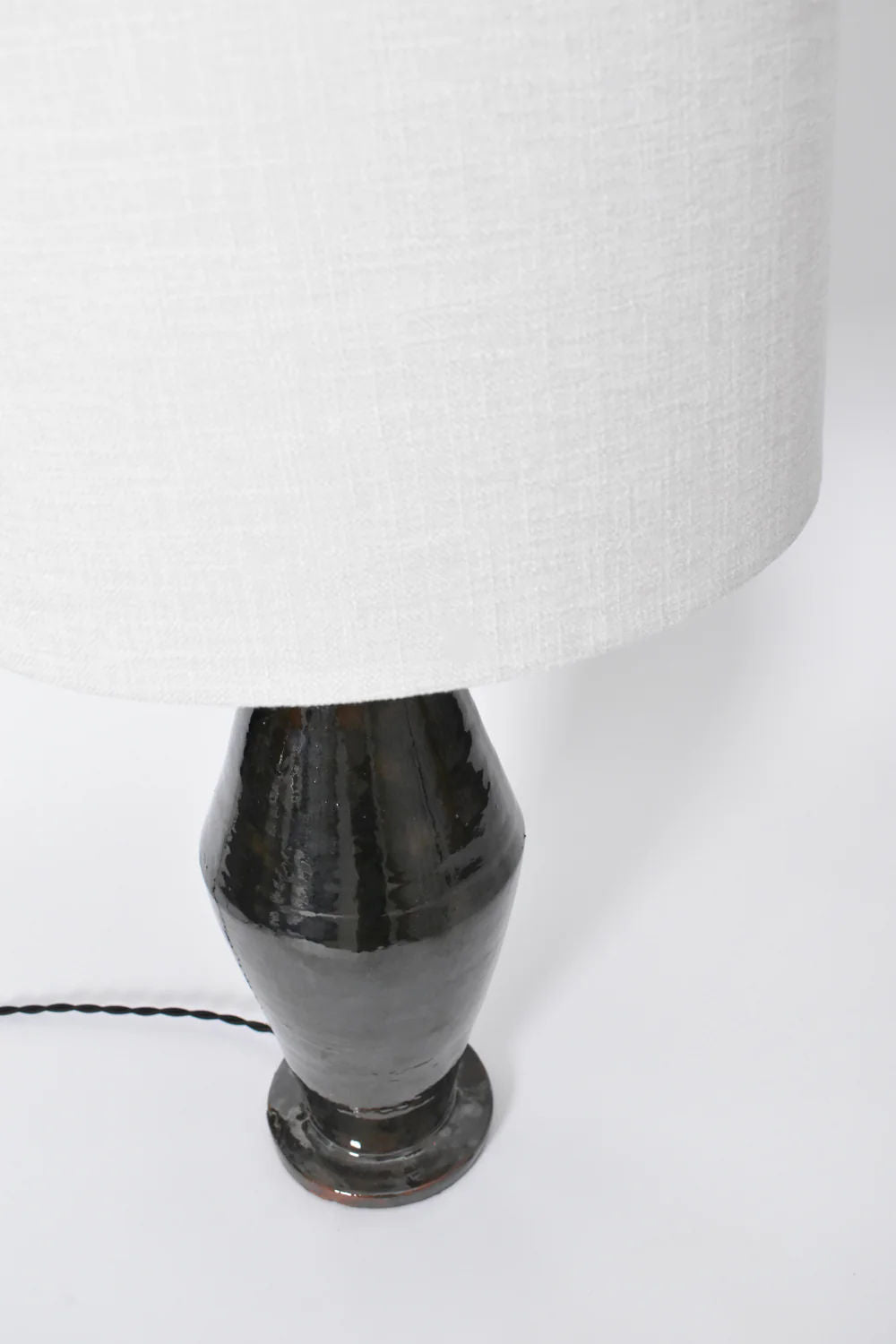 A close-up of the "Arrabida" Green Table Lamp by Barracuda Interiors shows its textured white shade and glossy dark green ceramic base, made in Portugal, with a black cord extending from the lamp on a white surface.