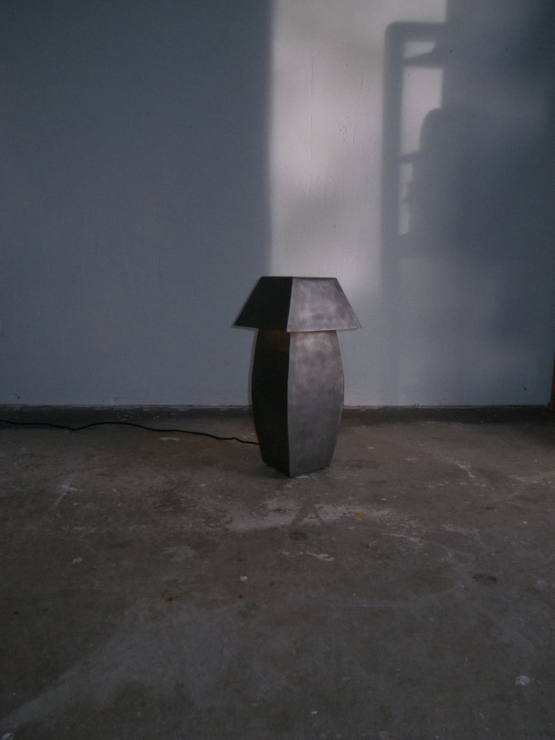 Tall hammered steel table lamp with conical shade in moody setting