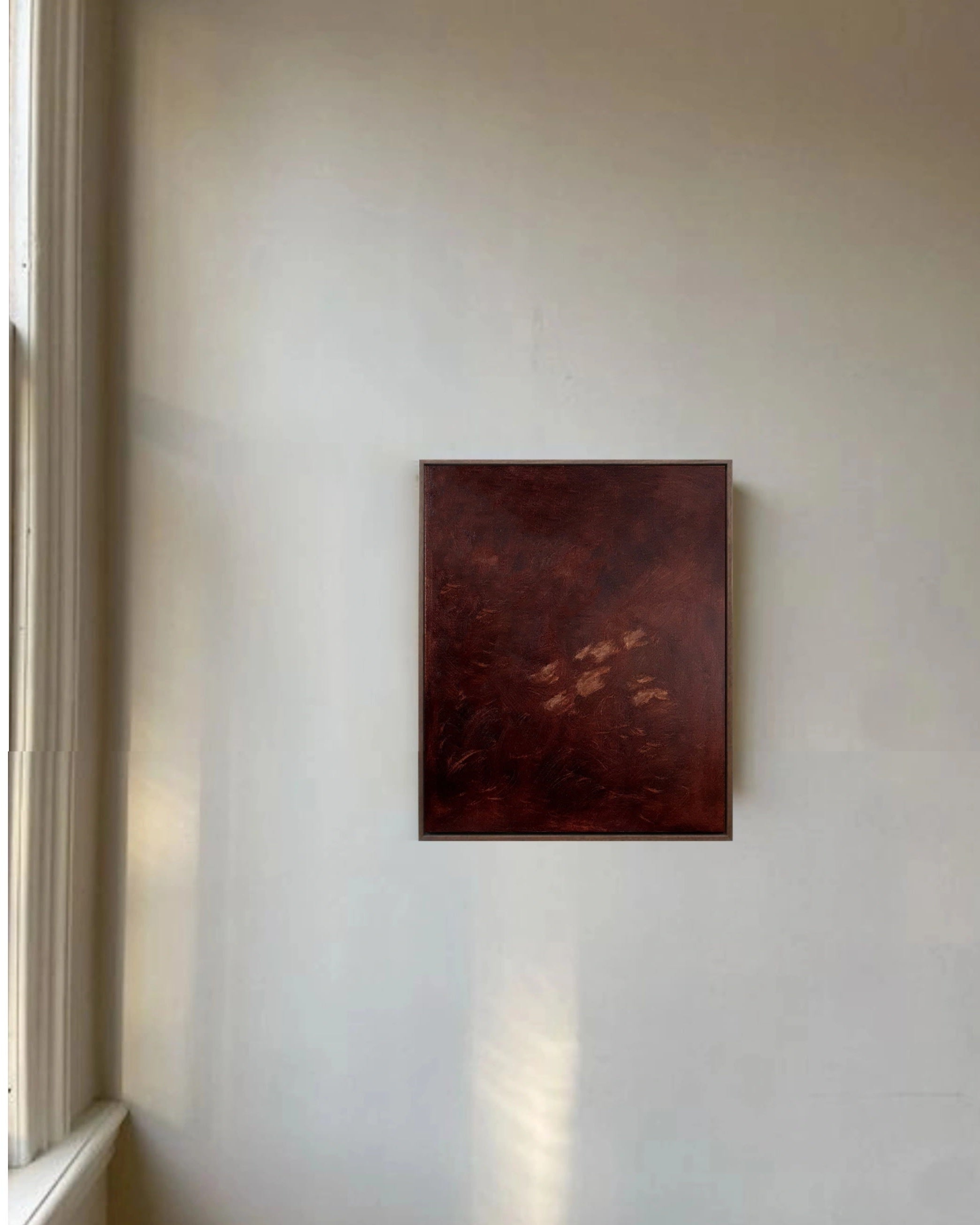 The 'Jane Eyre II' Painting by Yeliza Gevorgyan, a dark abstract oil on linen with reddish-brown tones, is framed and displayed on a light wall near a sunlit window with white trim.