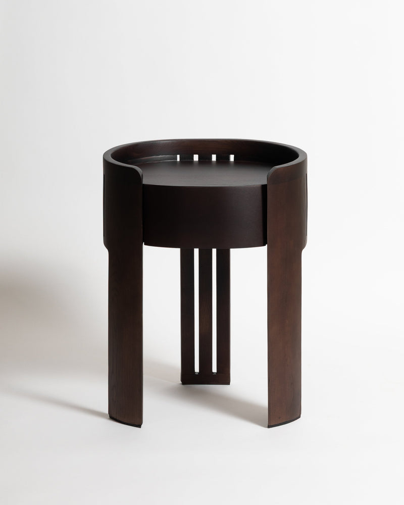 Dark wood round nightstand with cylindrical drawer and geometric legs by Tassiana Laurre