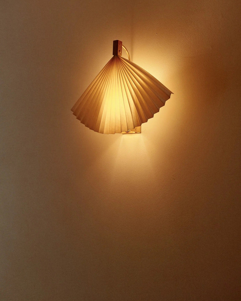 Fan-shaped pleated wall light creating warm ambient glow on wall