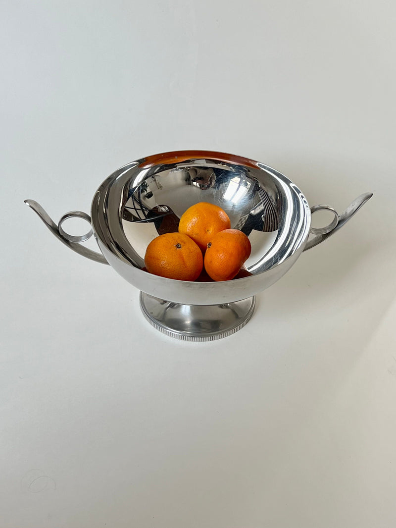 The Manushi Decorative Bowl With Handles in shiny silver, shown holding three small orange tangerines, is displayed against a plain white background.