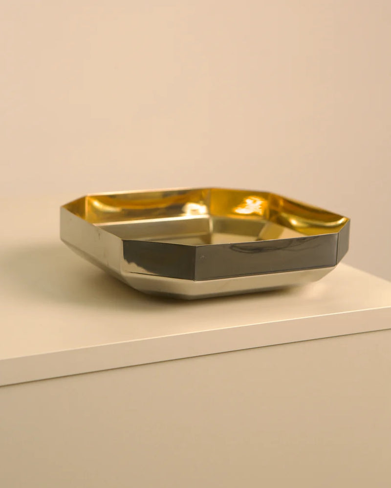 Golden metal vide-poche tray with curved edges on white shelf