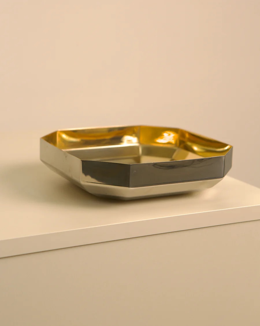 Golden metal vide-poche tray with curved edges on white shelf