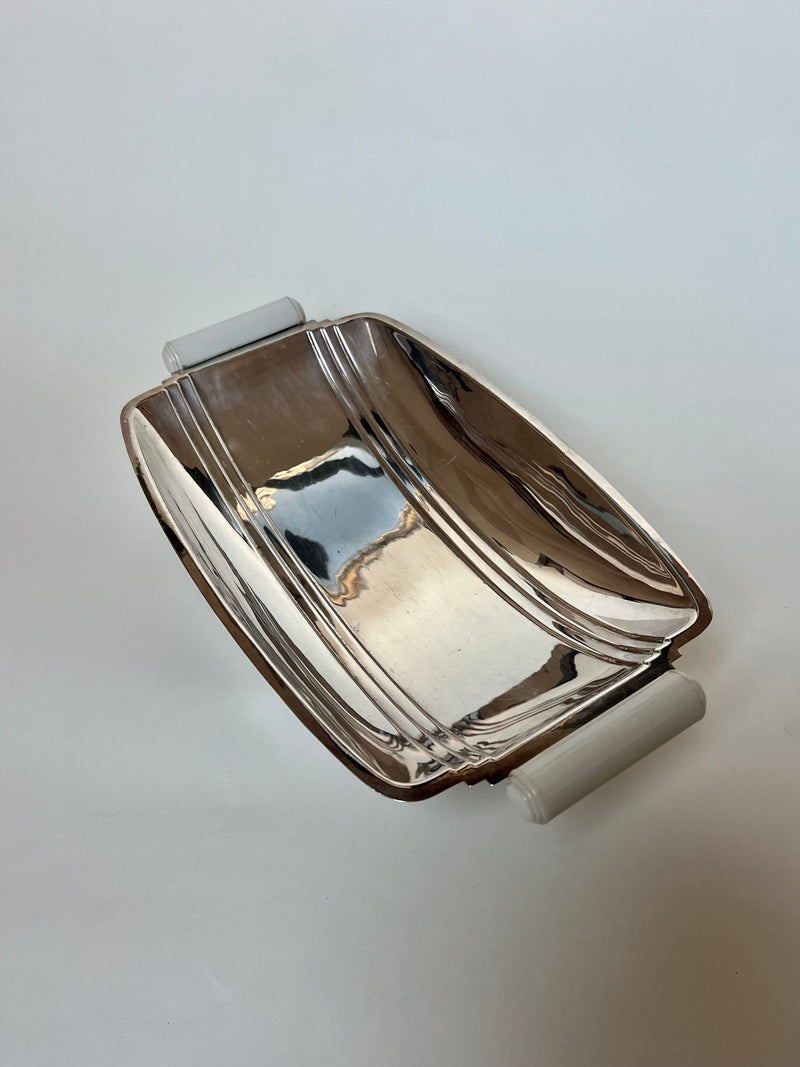 The Manushi Art Deco Bread Dish With Handles features a rectangular silver design with a modern, slightly curved Art Deco style and elegant lines, shown on a plain white background.