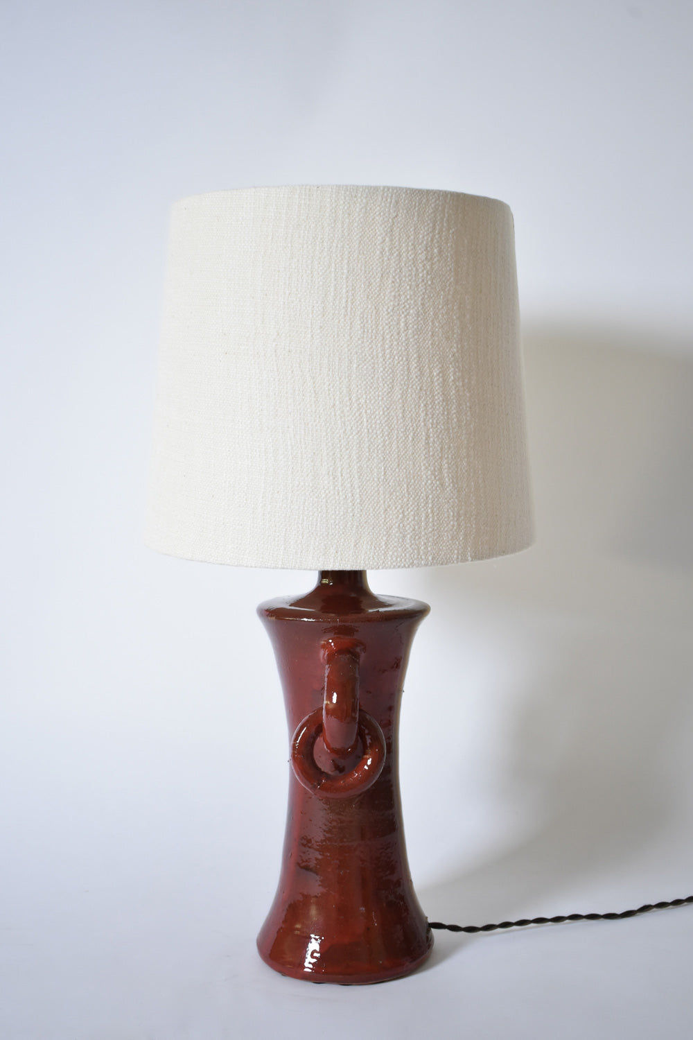 The "Kasaï" Red Handles Ceramic Table Lamp by Barracuda Interiors features a glossy reddish-brown circular base and a tall off-white fabric shade. Made in Portugal, it’s shown against a plain white background.