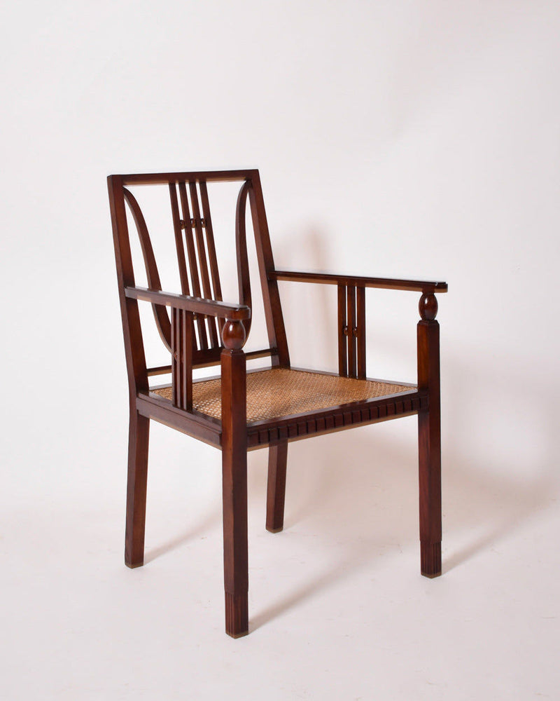 The Viennese Secession Armchair, 1910s by Barracuda Interiors features a wooden frame, decorative backrest, cane seat, straight legs, and carved details, echoing vintage style against a plain white background.