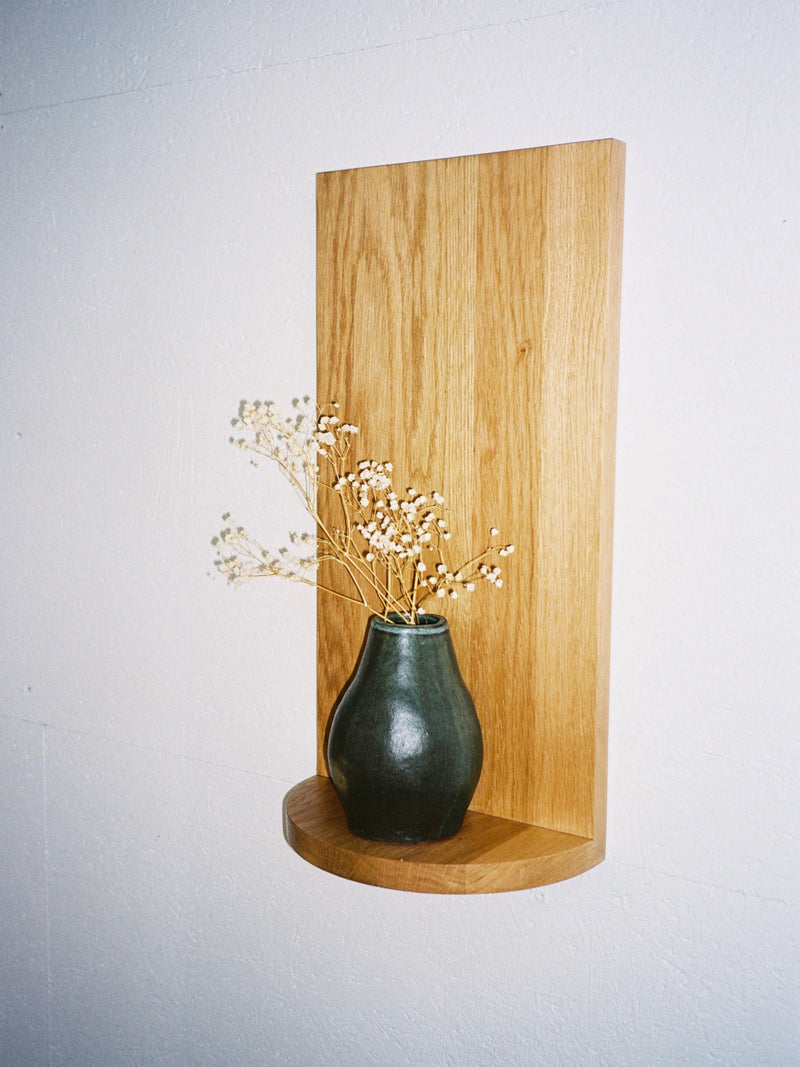 A small green ceramic vase with dried white flowers rests on The Megaron - Minimalist Shelf in Wood (Small) by COSEINCORSO, handcrafted and mounted on a white wall.