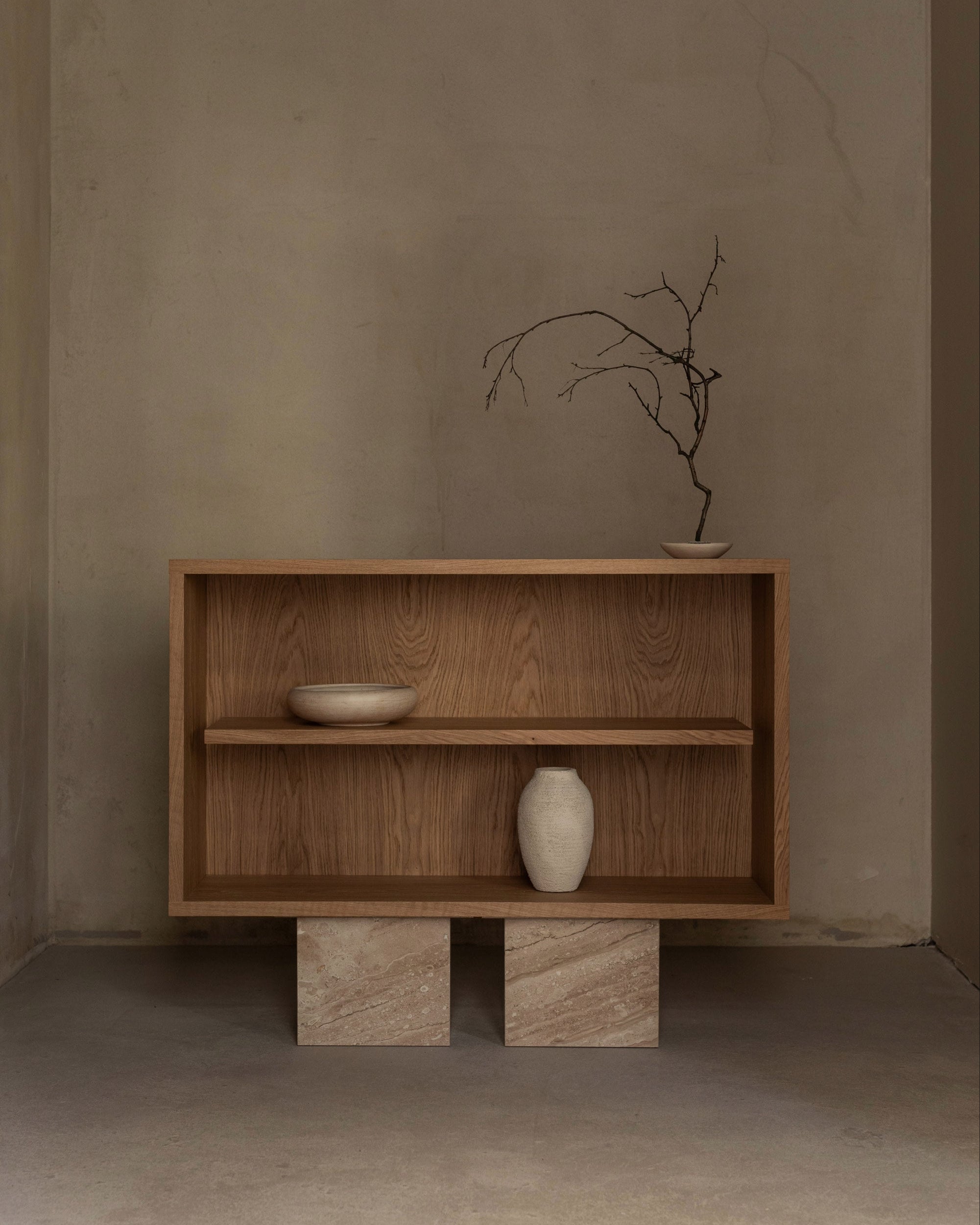The BLOCK Sideboard by un'common, with a minimalist wooden design on two stone blocks, is styled against a beige wall. Two ceramic vases—one with a bare branch—and a shallow bowl complete the elegant, simple look.