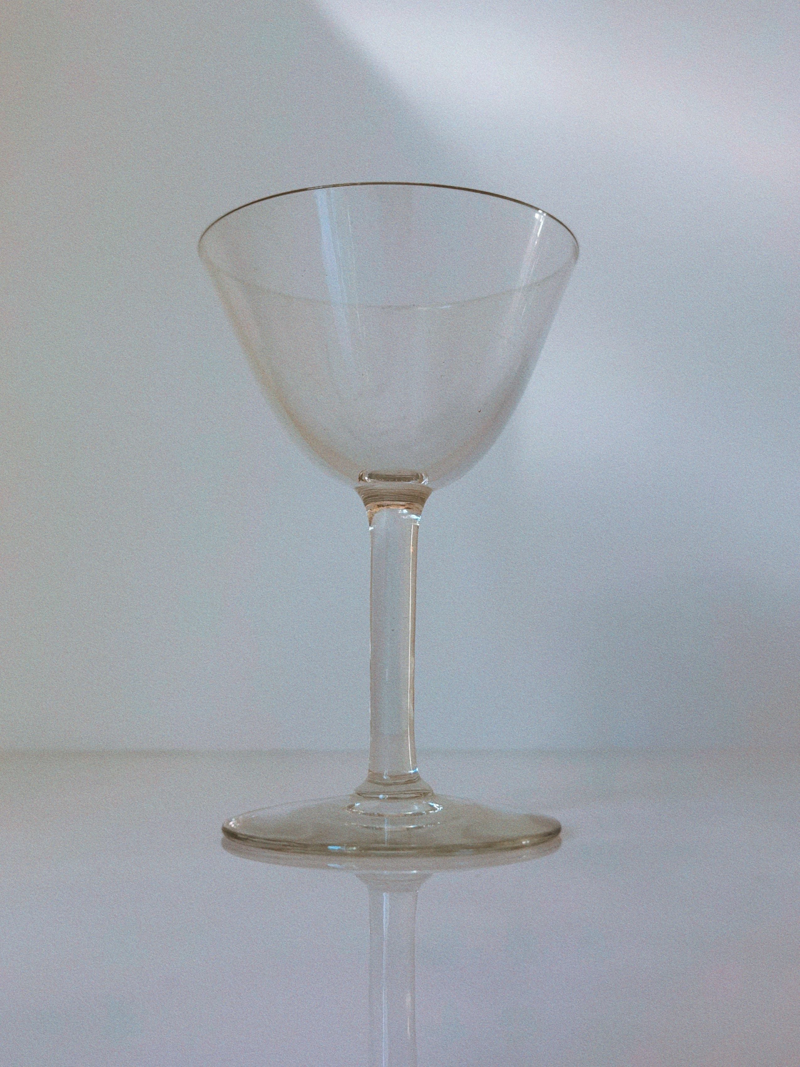 Clear Swedish cocktail glass with thin stem on reflective surface