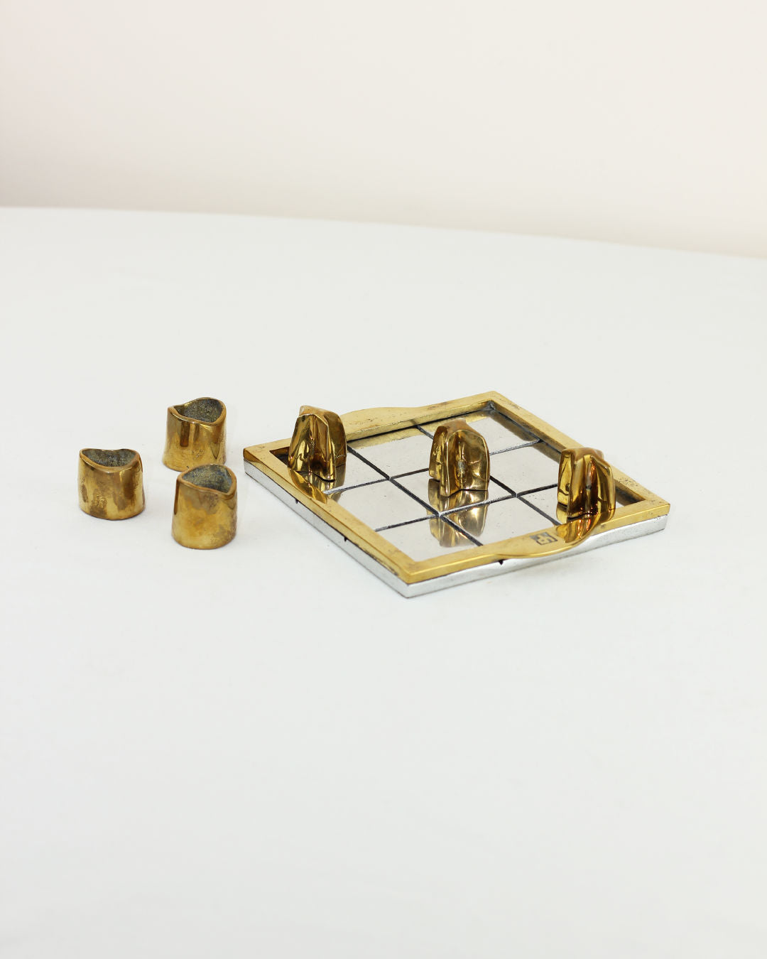 Brutalist Tic Tac Toe — angled view on white table with brass pieces