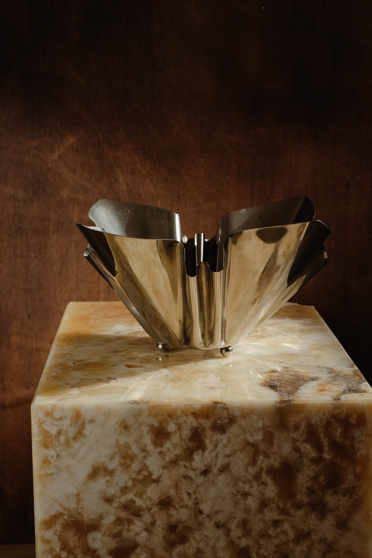 Folded Chrome Bowl — side angle on marble pedestal