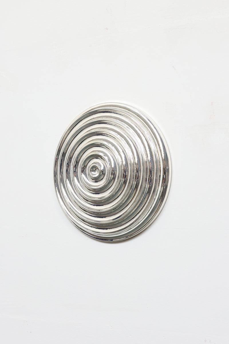 The Klaveroog by Studio Arno Hoogland is a shiny, wave chrome silver circular object with concentric raised rings, shown mounted on a plain white background.