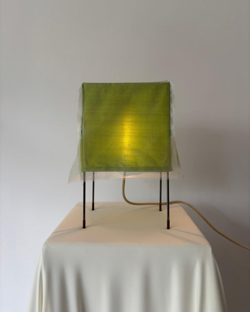 Green fabric table lamp with illuminated shade on metal legs