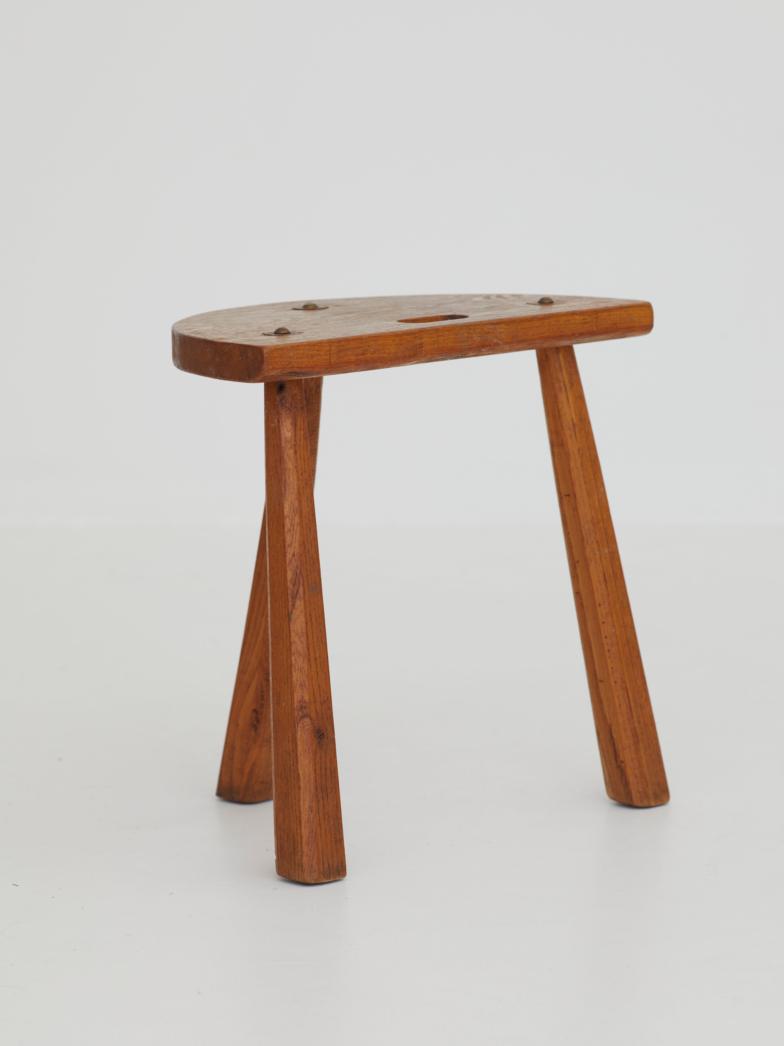 Two French Artisanal Solid Wood Half-moon Tripod Stools, Circa 1950 — angled view highlighting wooden texture and legs