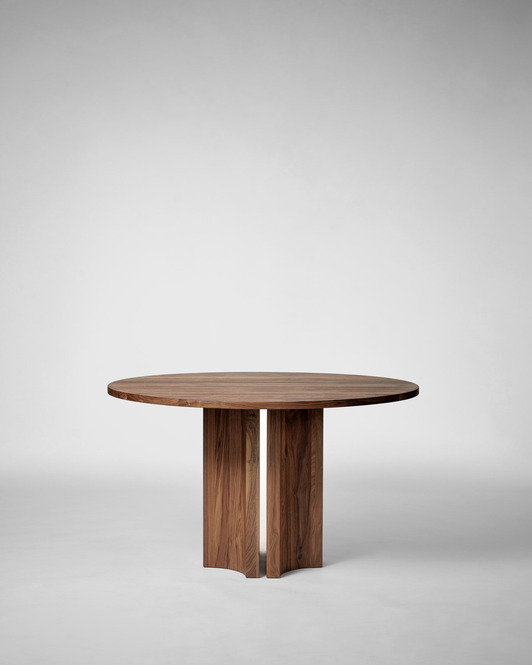 Round walnut dining table with crossed pedestal base by Mokko