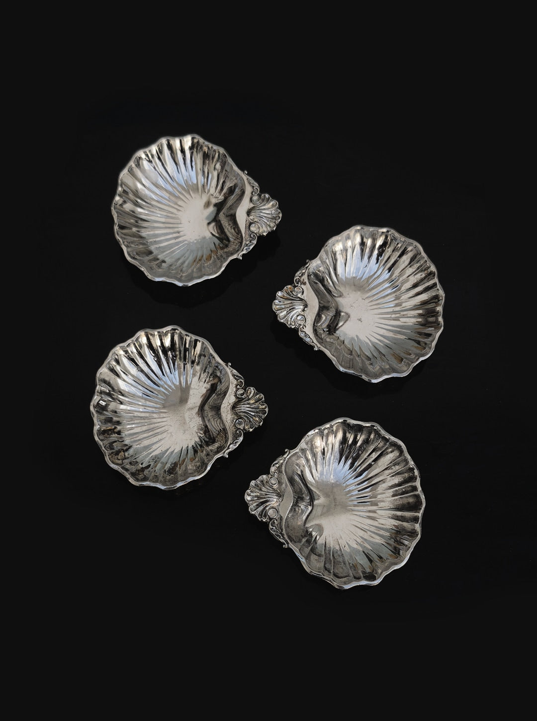 Set of 4 small shell vide poches by Les Objoies, silver-plated with ornate handles. Each fluted dish is ideal for decorative display or as a sophisticated catchall, shown arranged on a black background.