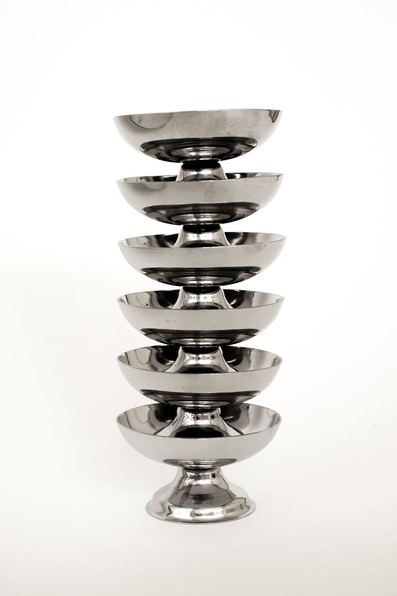 A set of six shiny, metallic ice coupes by septembre studios is stacked vertically against a white background, highlighting this elegant glassware collection.