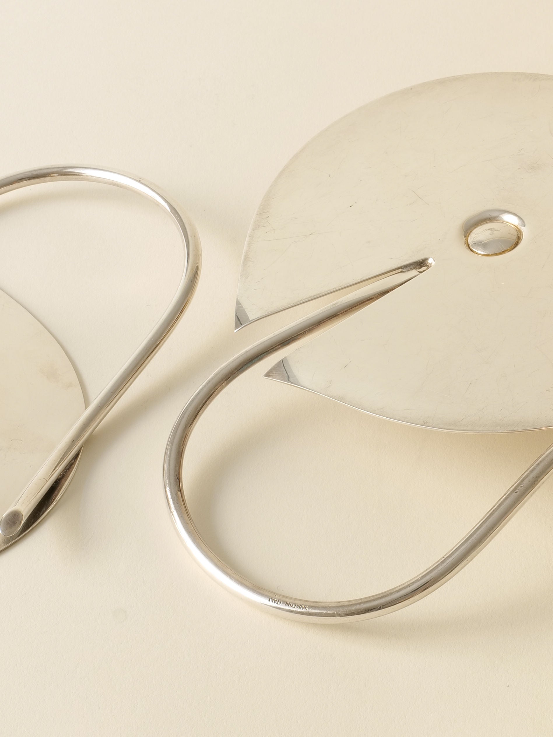 Two Candle Holder Lino Sabattini 1970s by Collection apart, with sleek curved design and metallic finish, rest diagonally on a light surface. Their stylish look evokes modern Italian elegance.