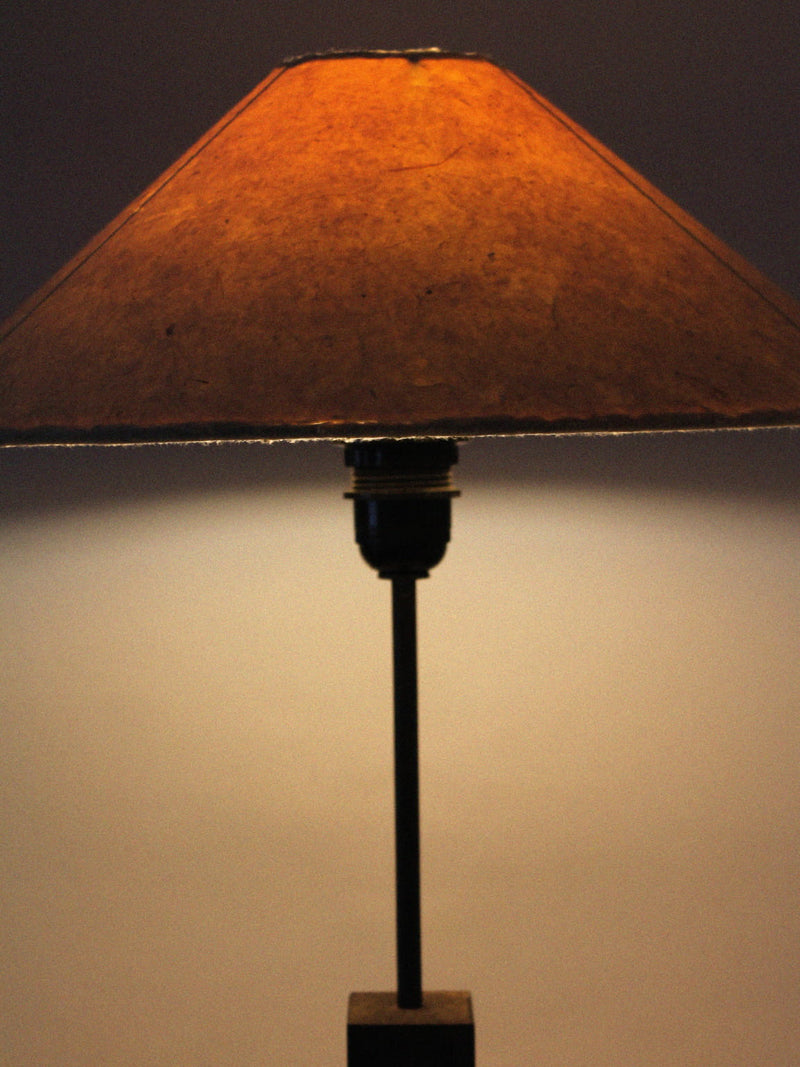 The Vintage Stories Mid-Century Swedish Wood And Iron Tall Lamp features a wide brown textured paper shade and dark wood and iron base, casting a warm, soft glow against a neutral background.