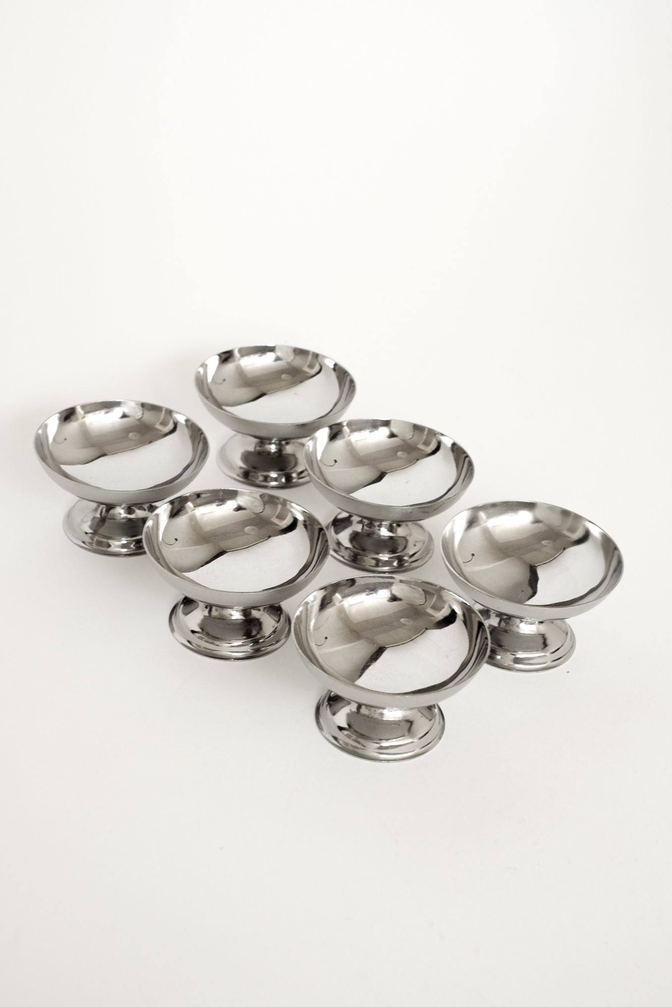 A set of six shiny stainless steel ice coupes from septembre studios is arranged on a plain white background, ideal for serving desserts or cocktails.